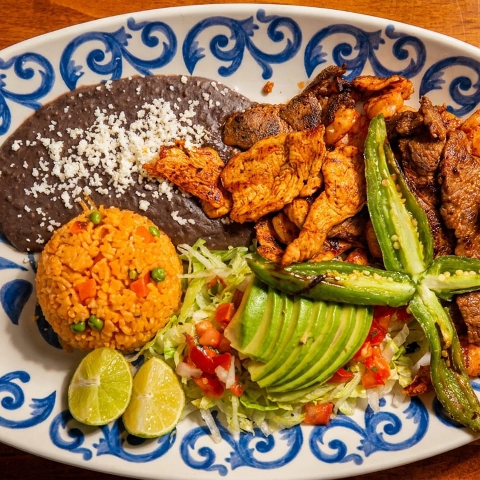 A colorful Mexican platter with grilled chicken, steak, shrimp, rice, beans, avocado, and jalapeños.
