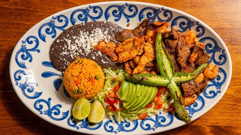 A colorful Mexican platter with grilled chicken, steak, shrimp, rice, beans, avocado, and jalapeños.