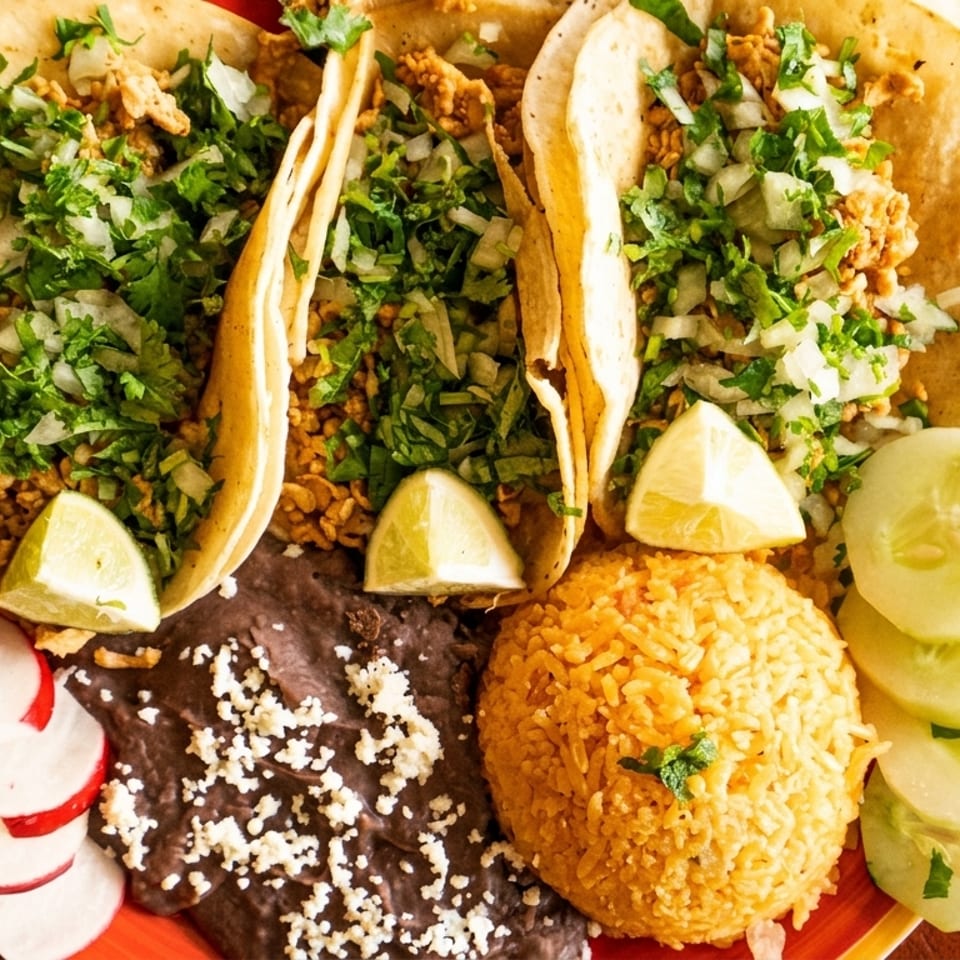 Three tacos with cilantro, onions, lime, rice, black beans, radishes, and cucumbers on a plate.