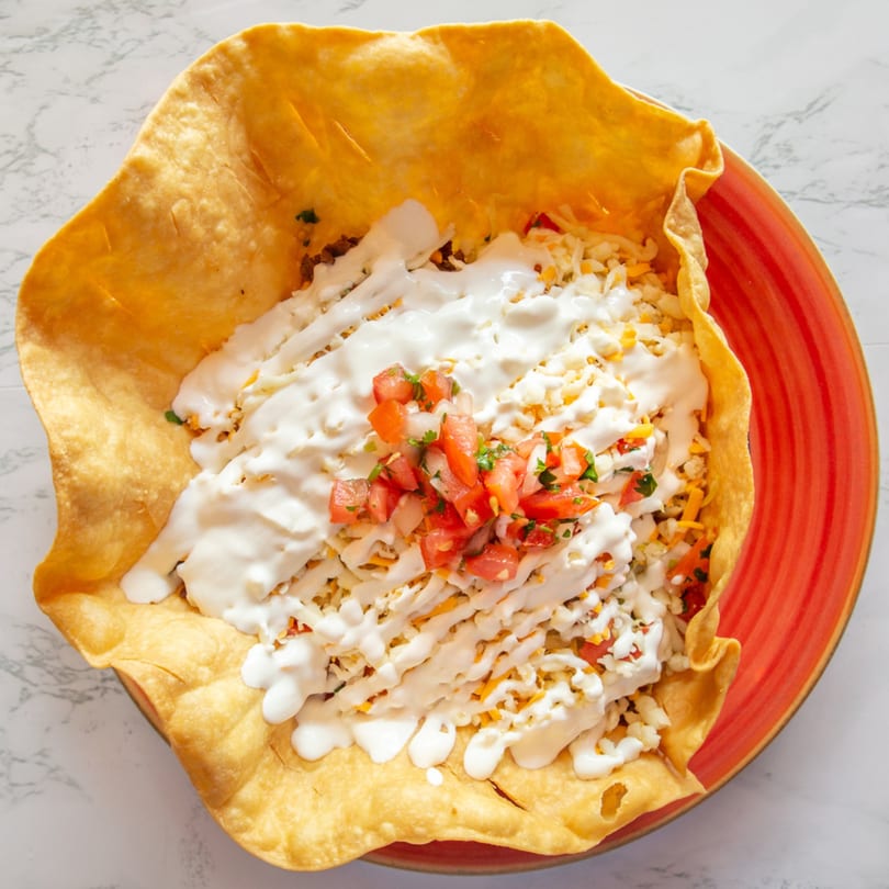 A Guilli's Mexican taco salad in a crispy tortilla bowl, topped with sour cream, cheese, and pico de gallo.