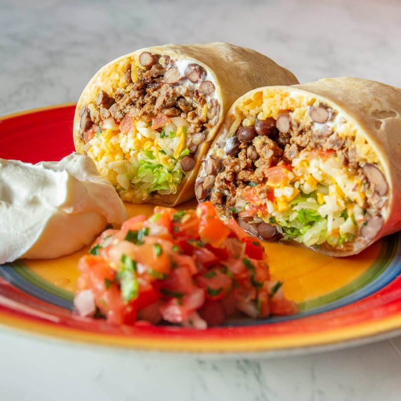 Two halves of a Guilli's burrito, filled with meat, beans, rice, lettuce, and cheese, with salsa and sour cream.
