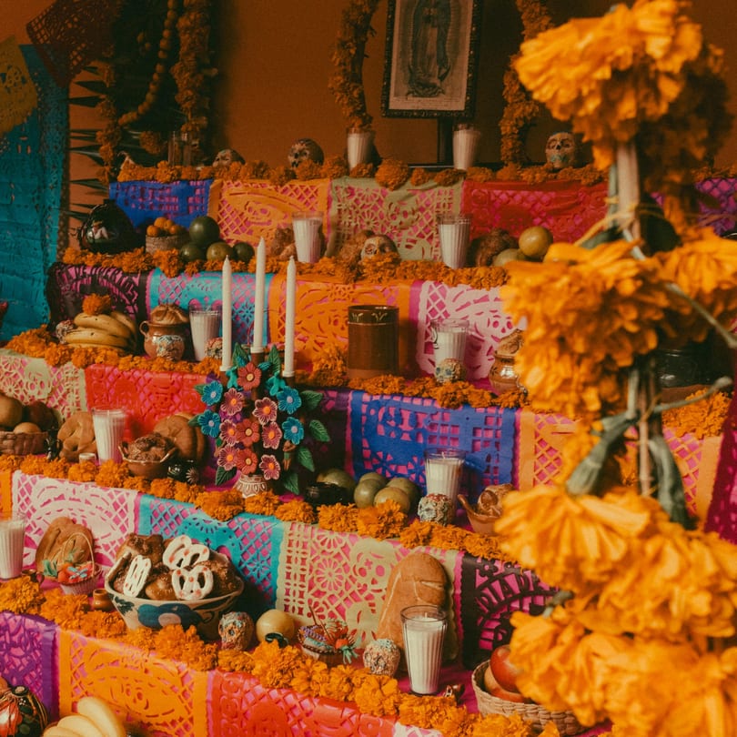 A vibrant Day of the Dead altar with marigolds, candles, food, and colorful papel picado.