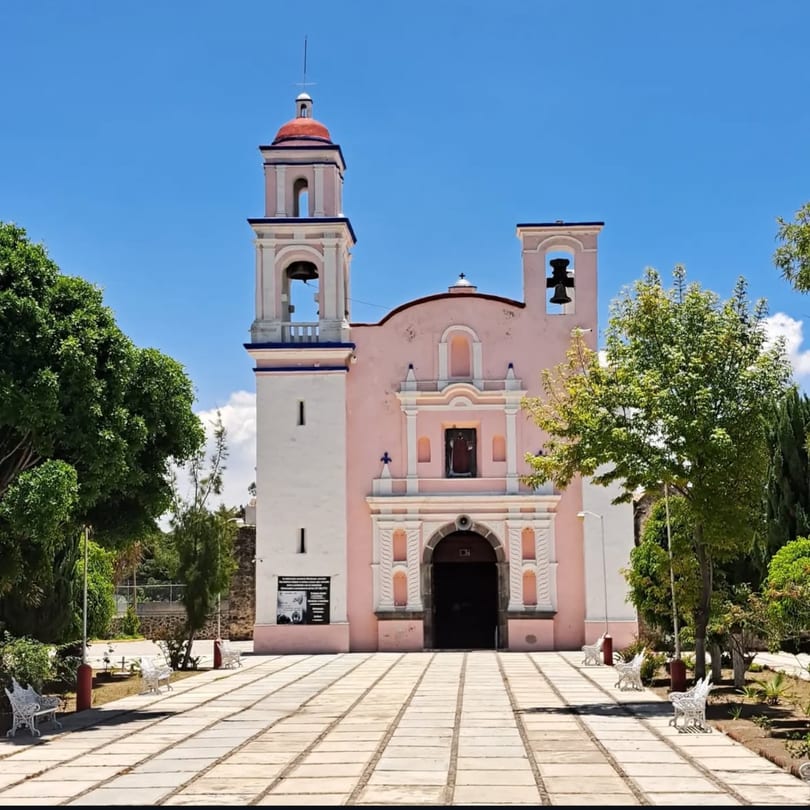 Pink and white church with two bell towers, a red dome, and a stone path leading to its entrance.