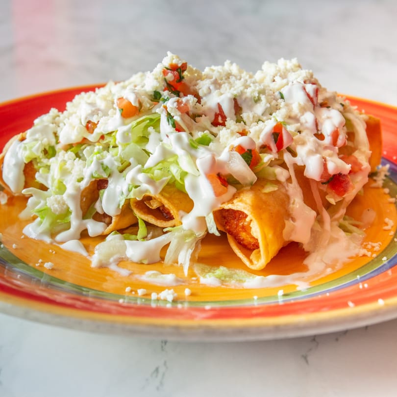 Guilli's taquitos topped with shredded lettuce, crumbled cheese, diced tomatoes, and sour cream.