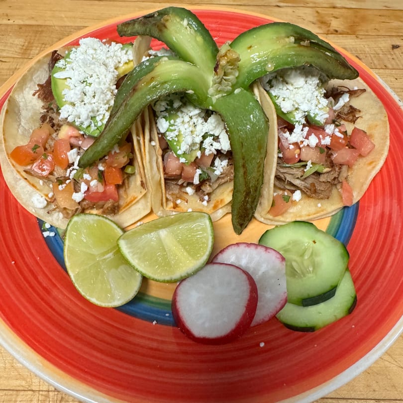 Three Guilli's Authentic Mexican Cuisine tacos with avocado, cheese, tomato, and lime on a colorful plate.